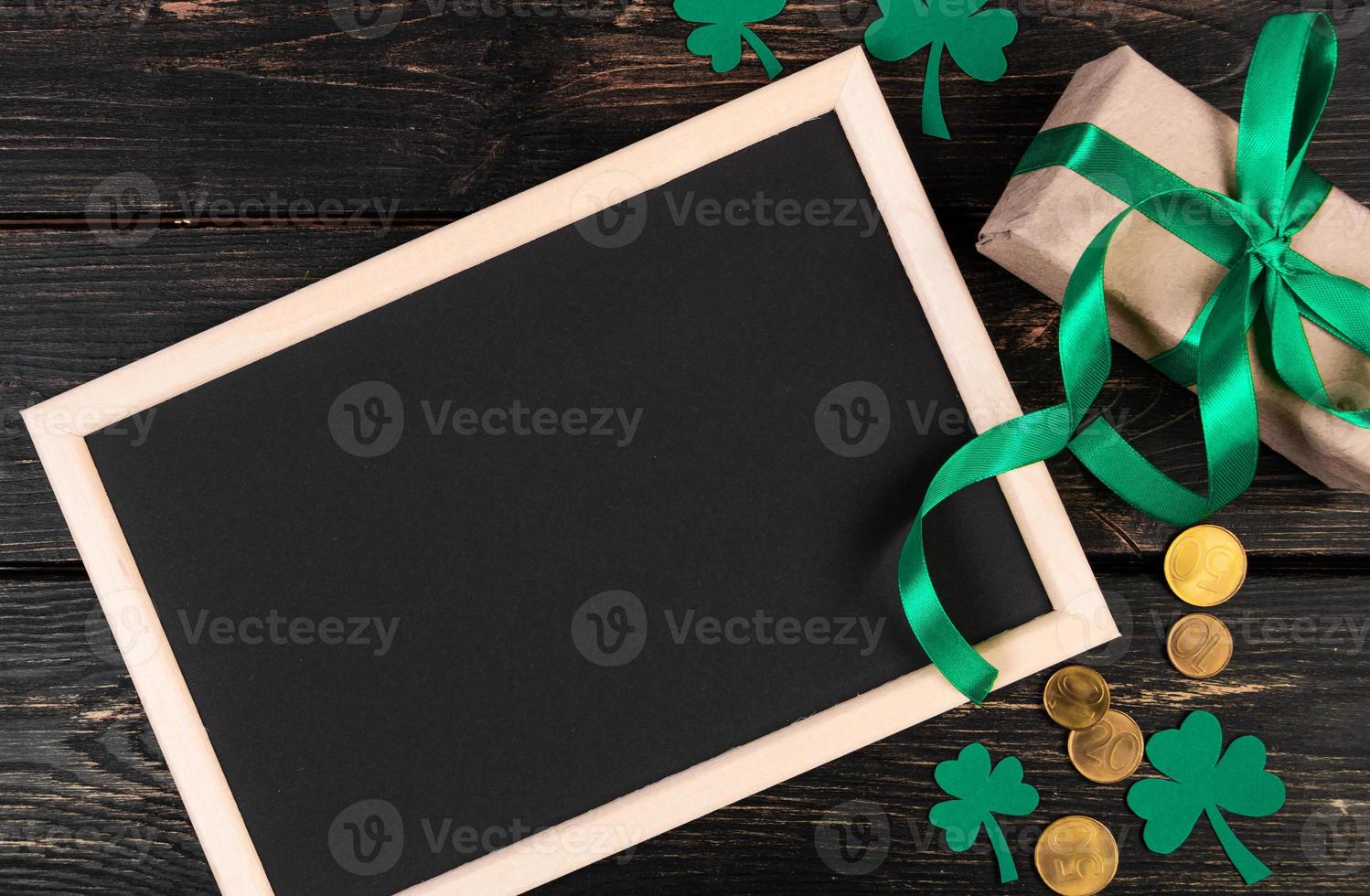 Clover shamrock, gold coins and gift with green ribbon on a brown wooden background. Festive composition. photo