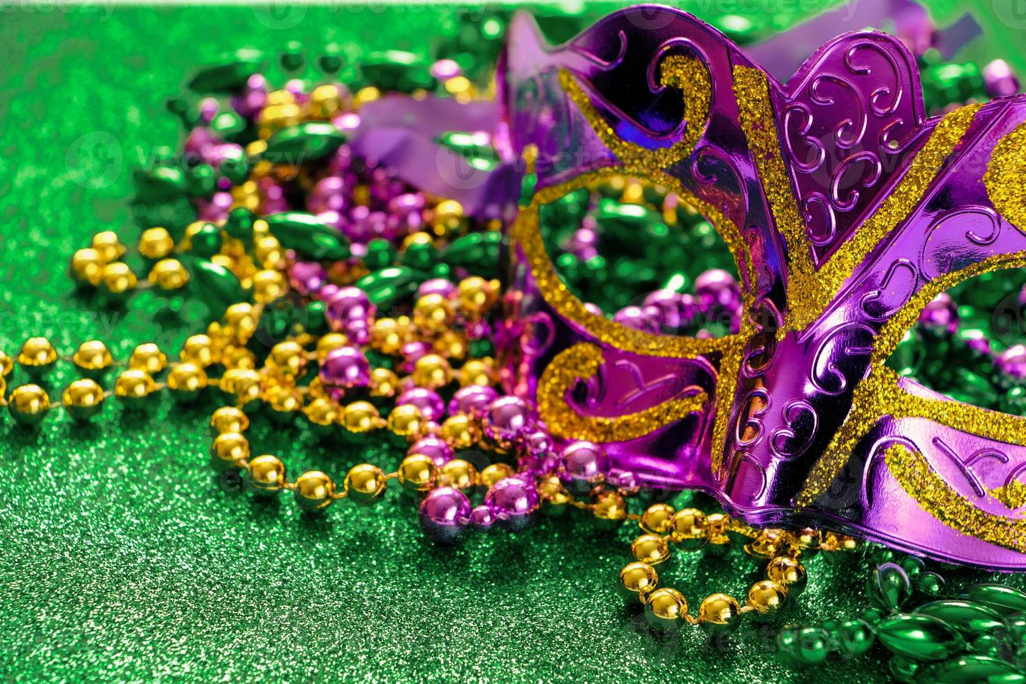 Carnival mask and colorful beads on green shiny background. Mardi Gras concept. photo