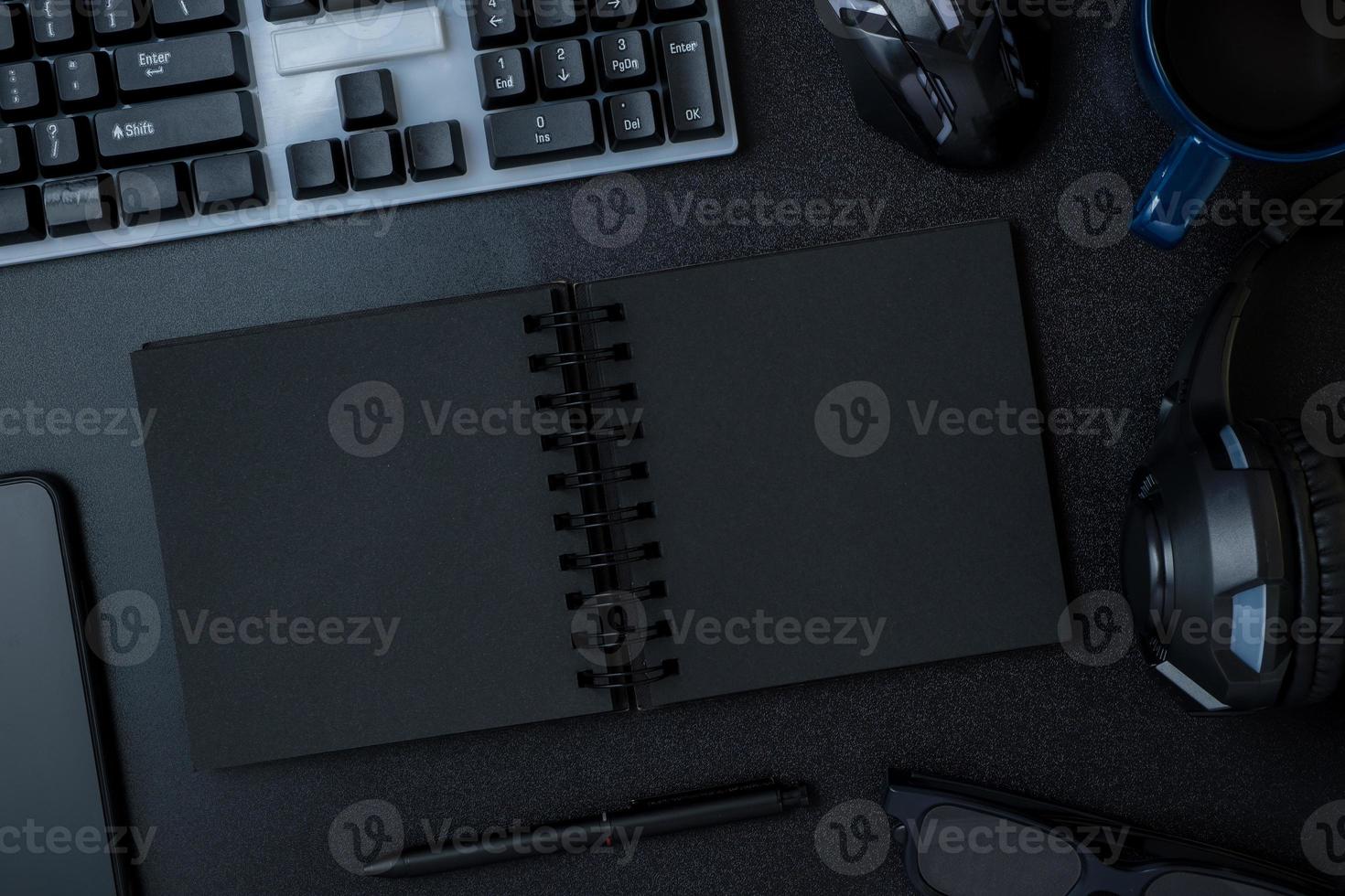 top view working desk with keyboard headphone and open notebook on black table background photo