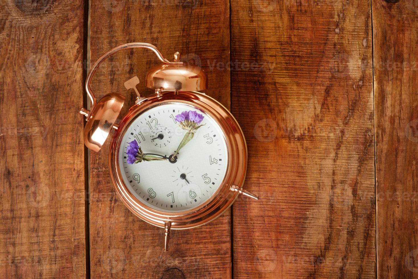 Vintage alarm clock made from gold metal with blue flowers instead of clock's hands on wooding surface. Spring time photo