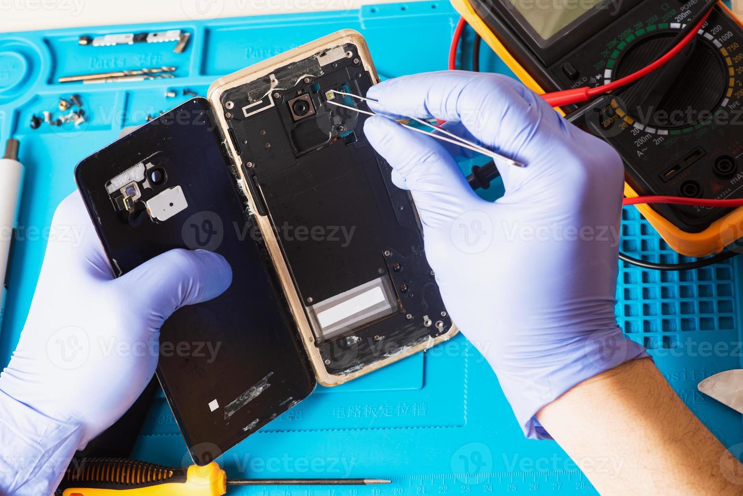 el artesano en guantes de goma repara o repara un teléfono móvil en una alfombrilla de goma especial para reparar. vista desde el interior foto