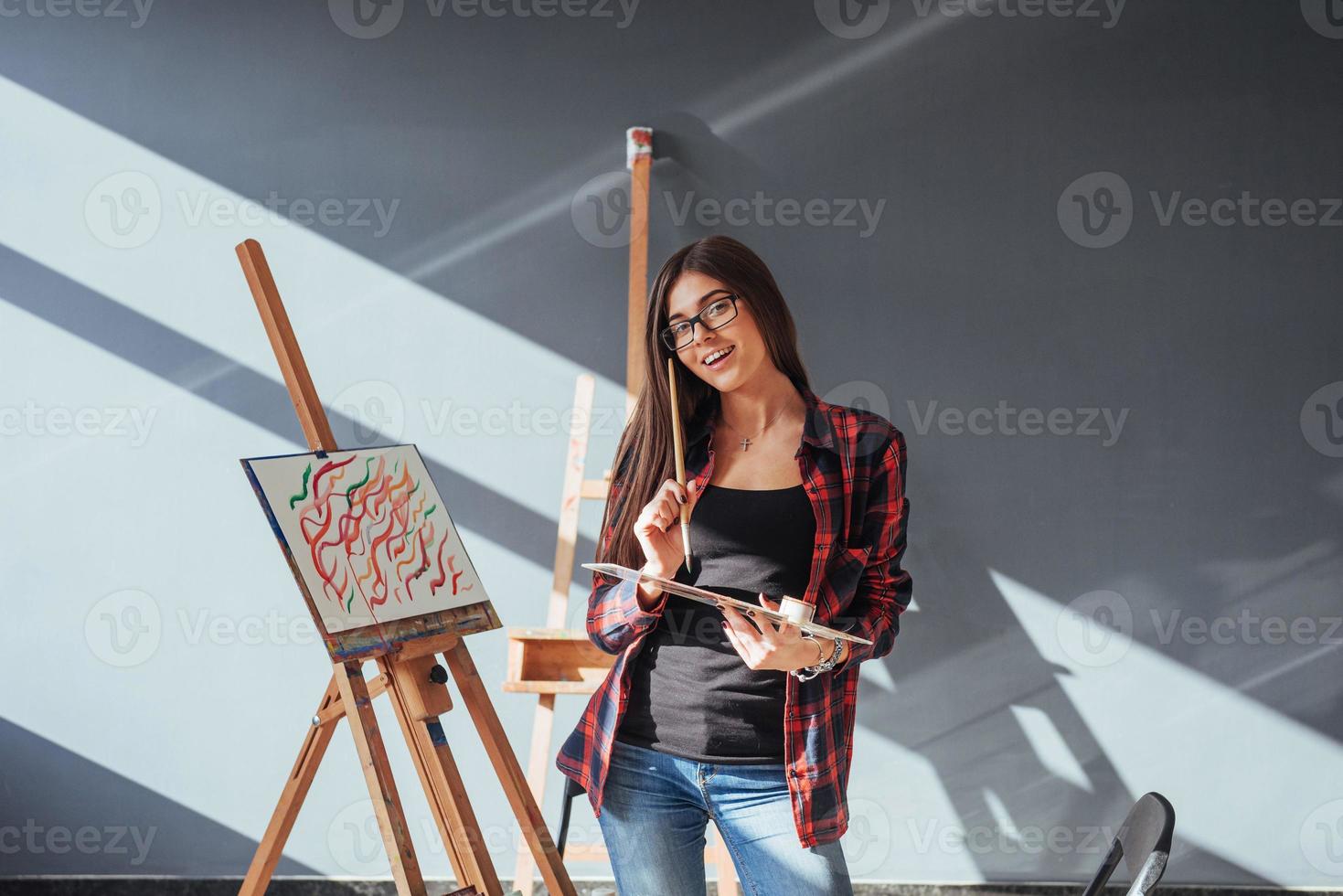 Creative pensive painter girl paints a colorful picture on canvas with oil colors in workshop. photo