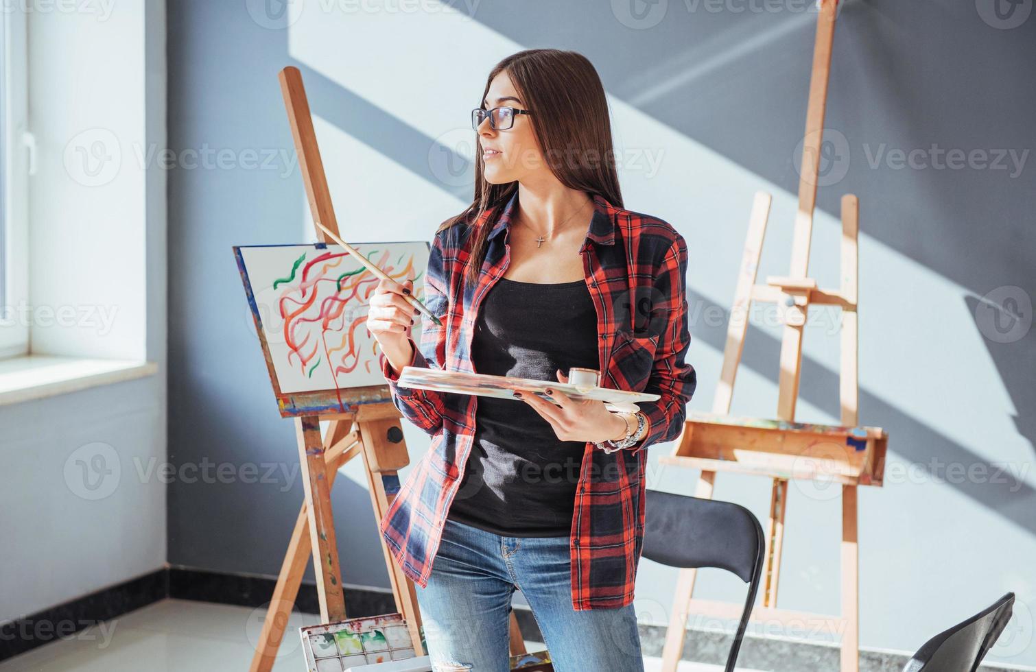 Creative pensive painter girl paints a colorful picture on canvas with oil colors in workshop. photo