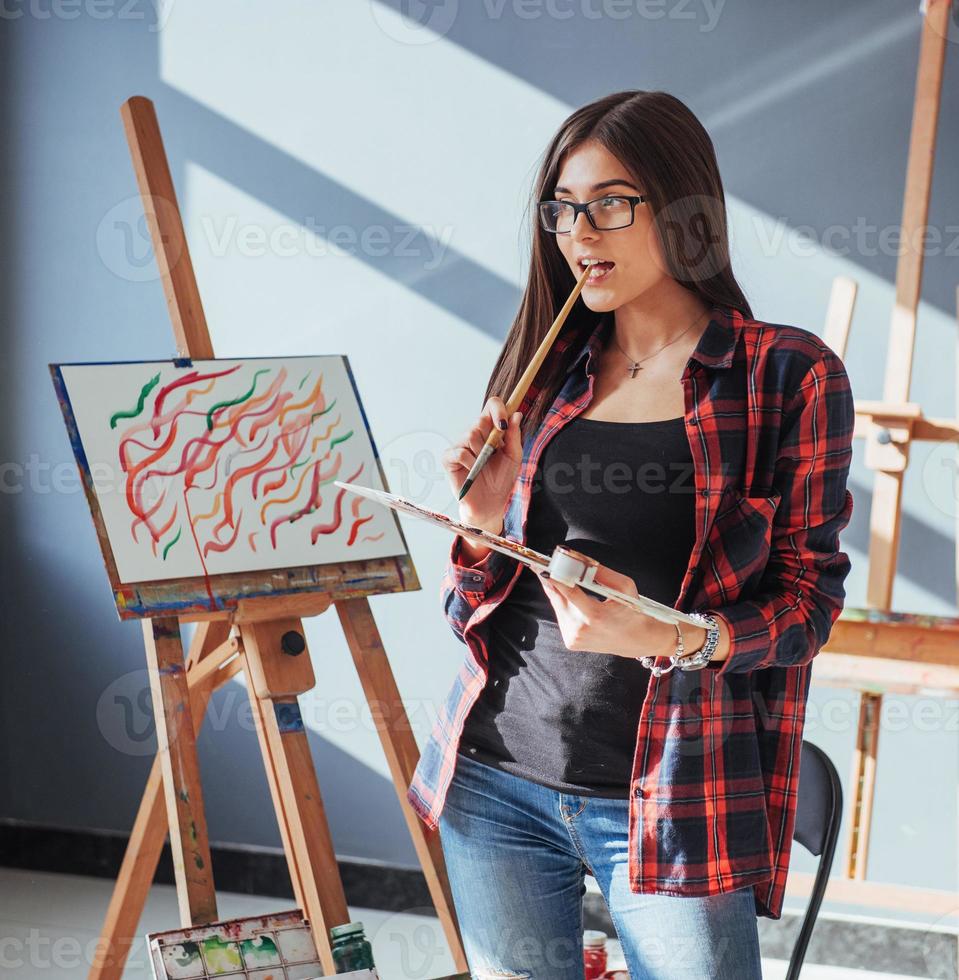 artista de pelo oscuro que sostiene un pincel en la mano y dibuja un cuadro sobre lienzo. piensa que se basa en foto