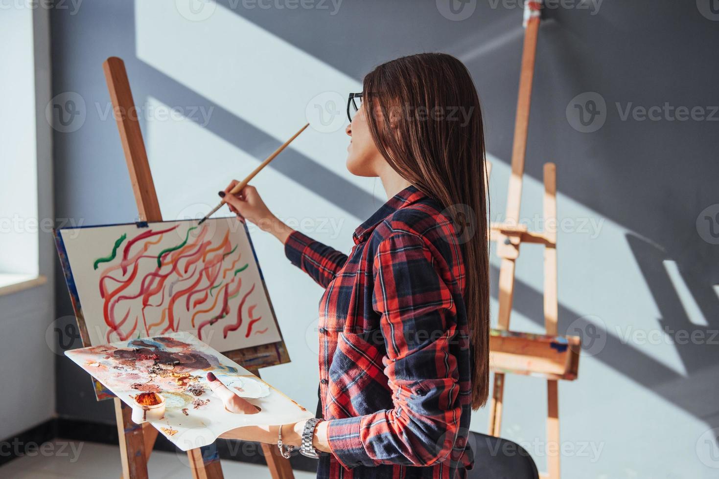 Creative pensive painter girl paints a colorful picture on canvas with oil colors in workshop. photo
