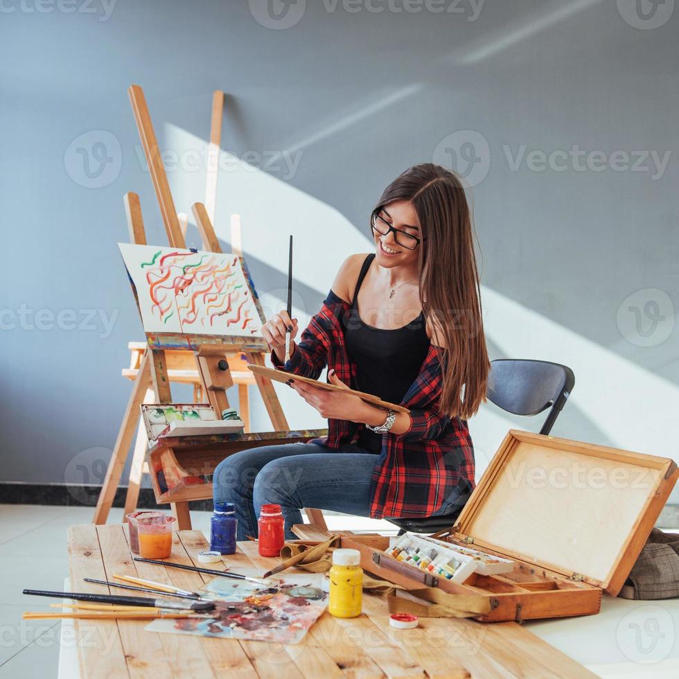 Creative pensive painter girl paints a colorful picture on canvas with oil colors in workshop photo