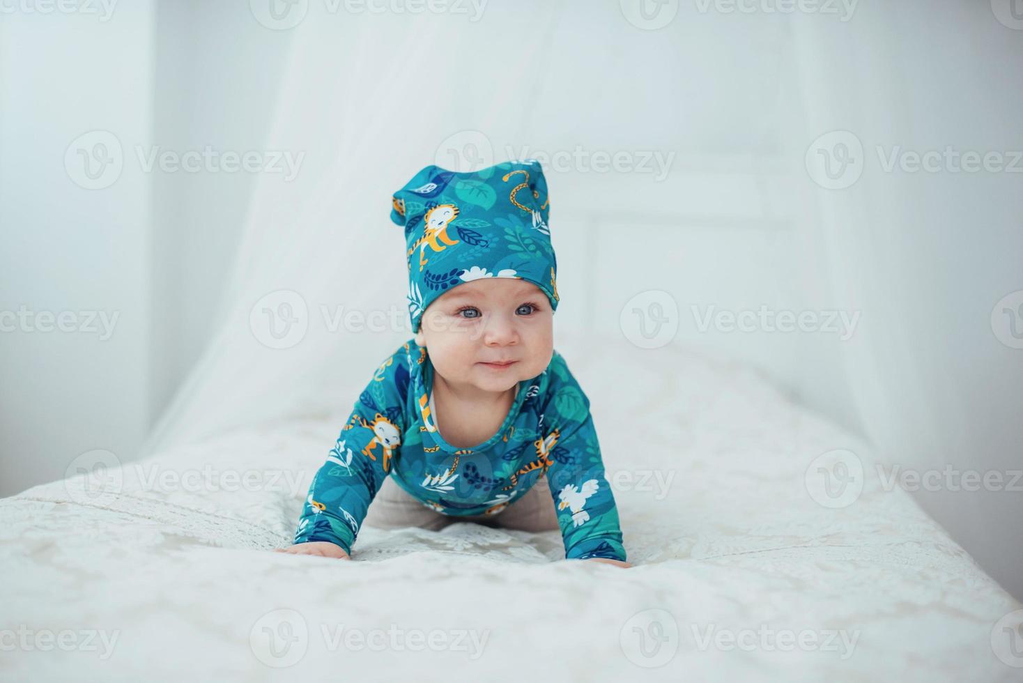 Newborn baby dressed in a green suit lying on a soft bed in a white studio. photo