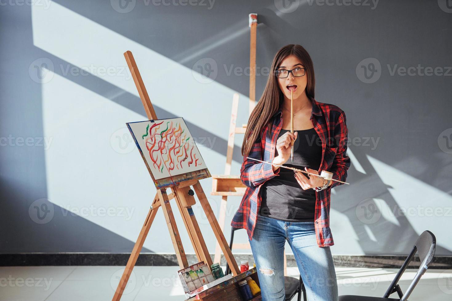 Creative pensive painter girl paints a colorful picture on canvas with oil colors in workshop. photo