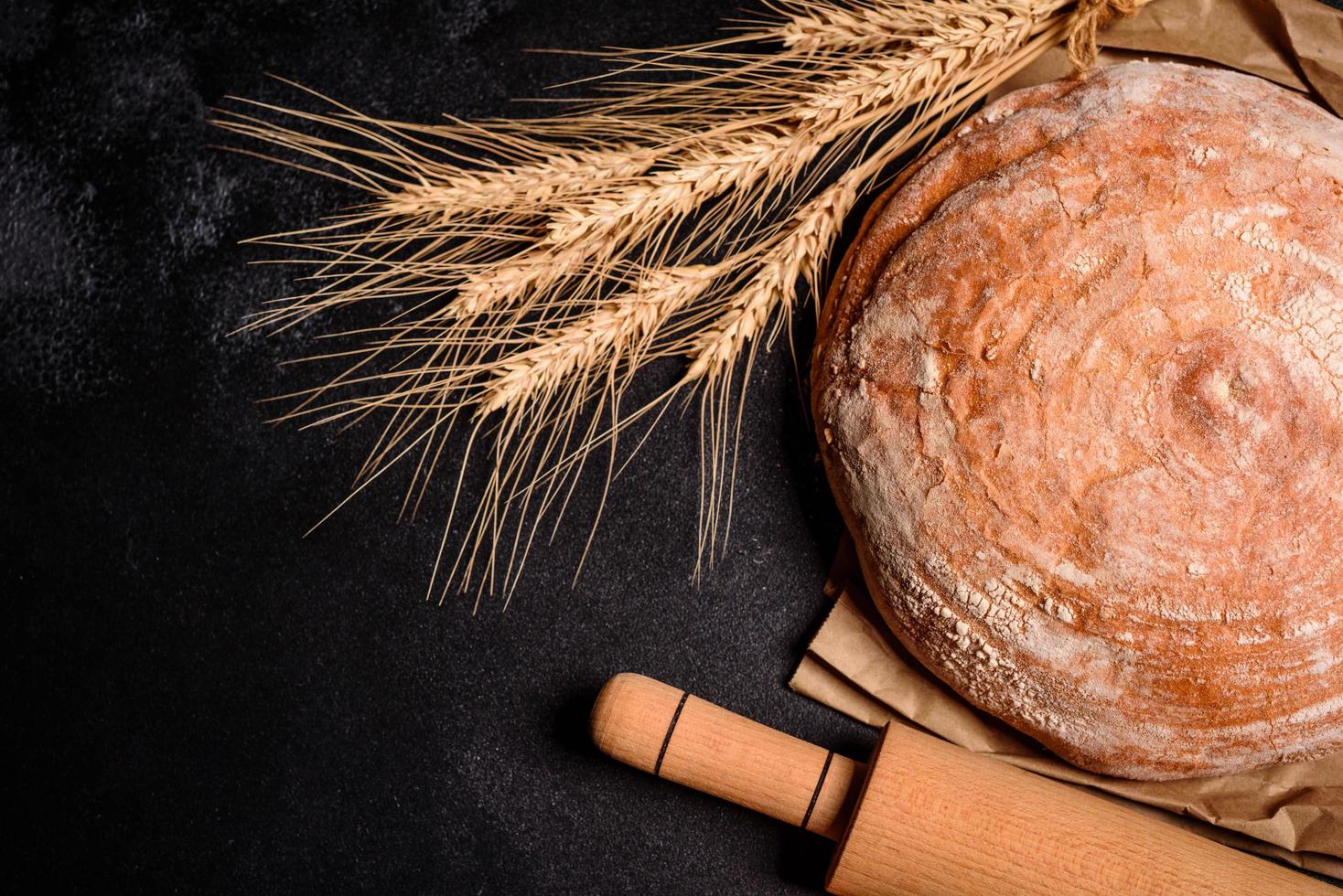 Beautiful fresh baked bread with wheat grains on a dark concrete background photo