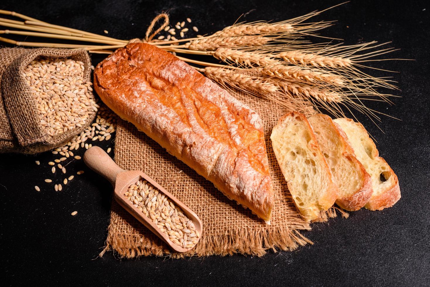 Beautiful fresh baked bread with wheat grains on a dark concrete background photo