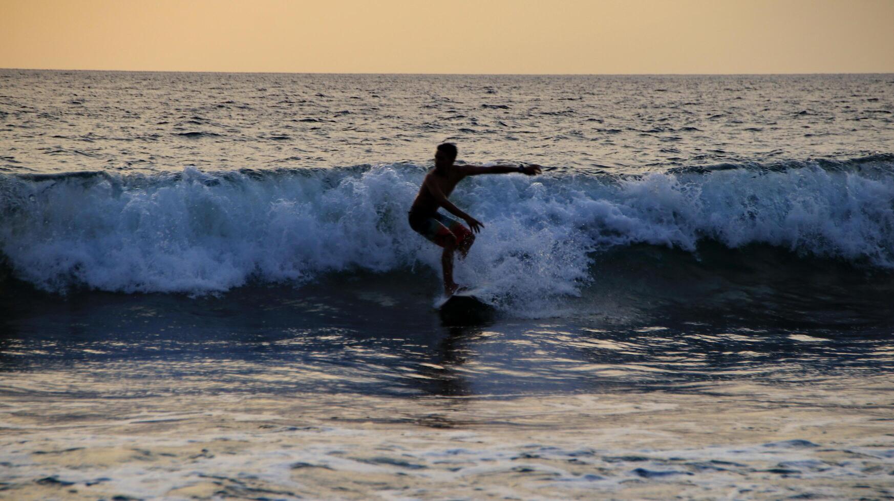 documentación de surfistas en acción al atardecer con un color dorado y oscuro, desenfocado y oscuro en la playa de senggigi lombok, oeste de nusa tenggara indonesia, 27 de noviembre de 2019 foto