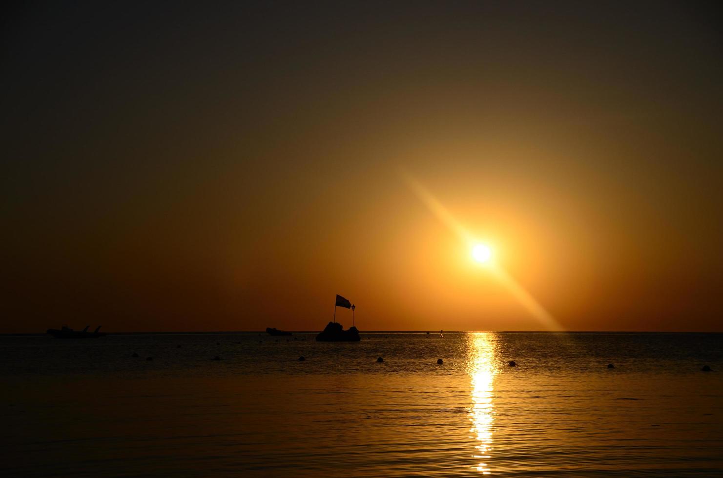 sunrise on sea with rocks and flag photo