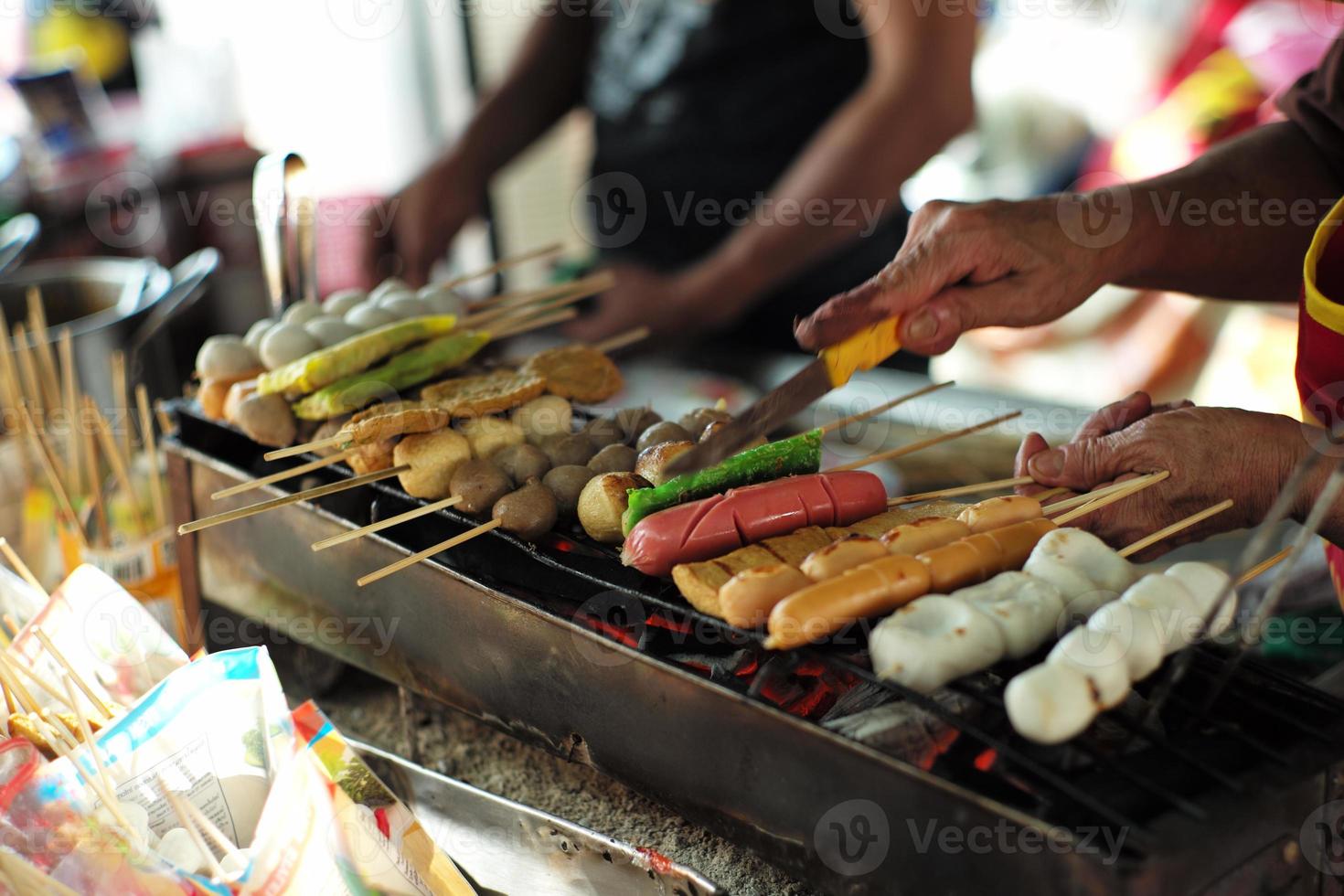 primer plano varios tipos de bolas y salchichas a la parrilla por el carbón con movimiento borroso de la mano en el fondo. comida de la calle foto