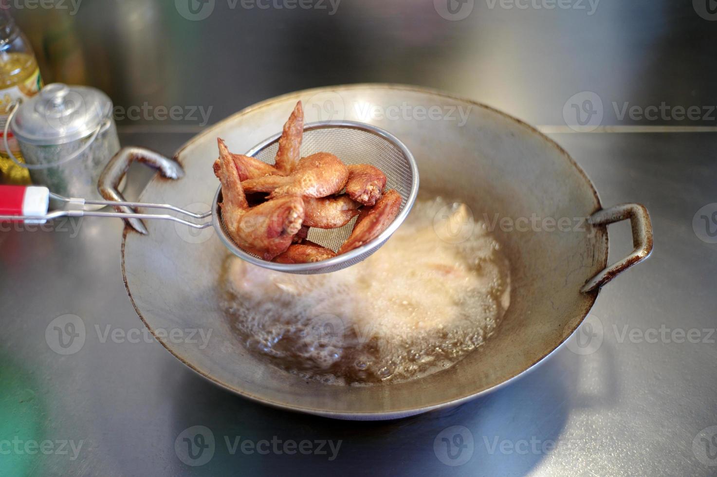 Closeup many pieces of deep fried chicken wings in te stainless basket with blurred boiled vegetable photo