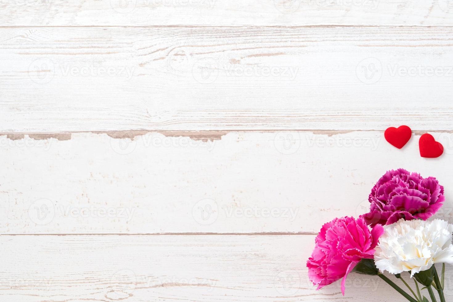 May mothers day concept photography - Beautiful carnations and hearts shape with white empty card isolated on a bright wooden table, copy space, flat lay, top view, mock up photo