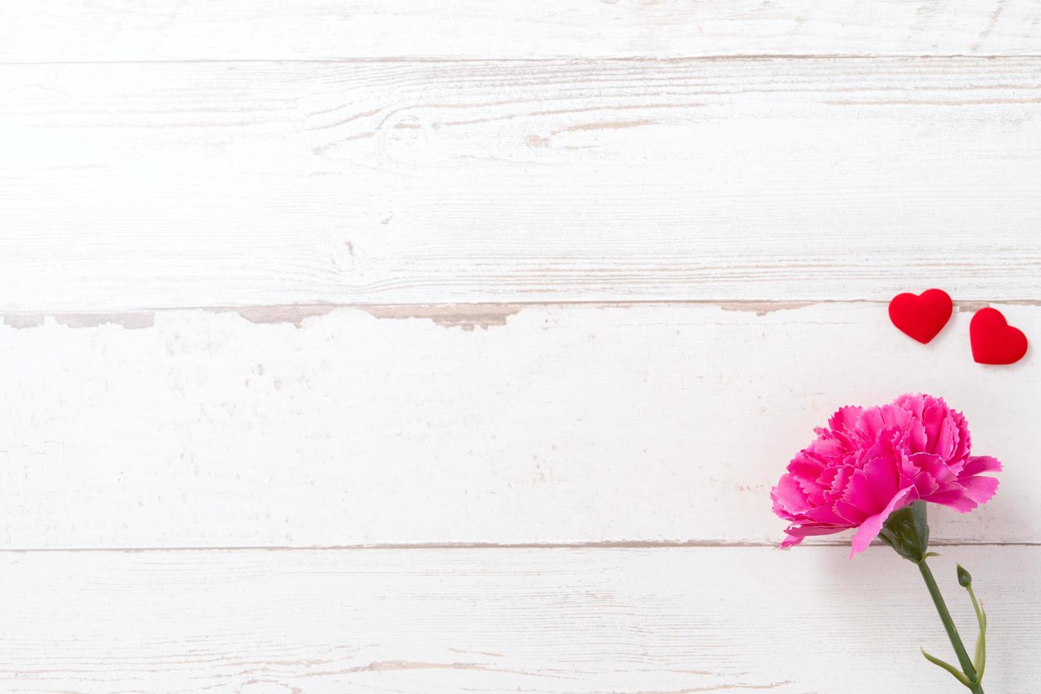 May mothers day concept photography - Beautiful carnations and hearts shape with white empty card isolated on a bright wooden table, copy space, flat lay, top view, mock up photo