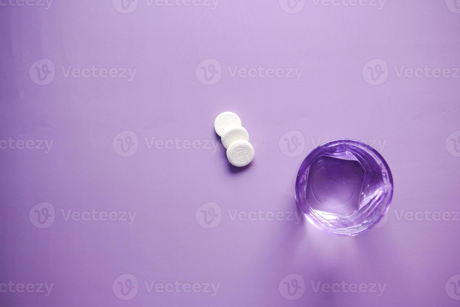 Effervescent soluble tablet pills and glass of water on purple background photo