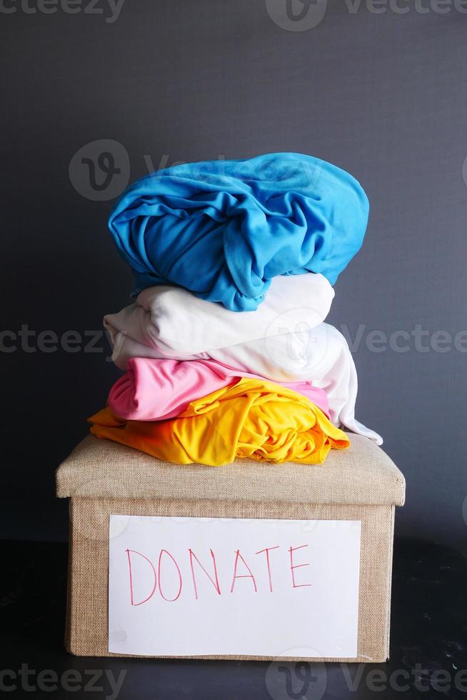 Donation box with stack of clothes against black background photo