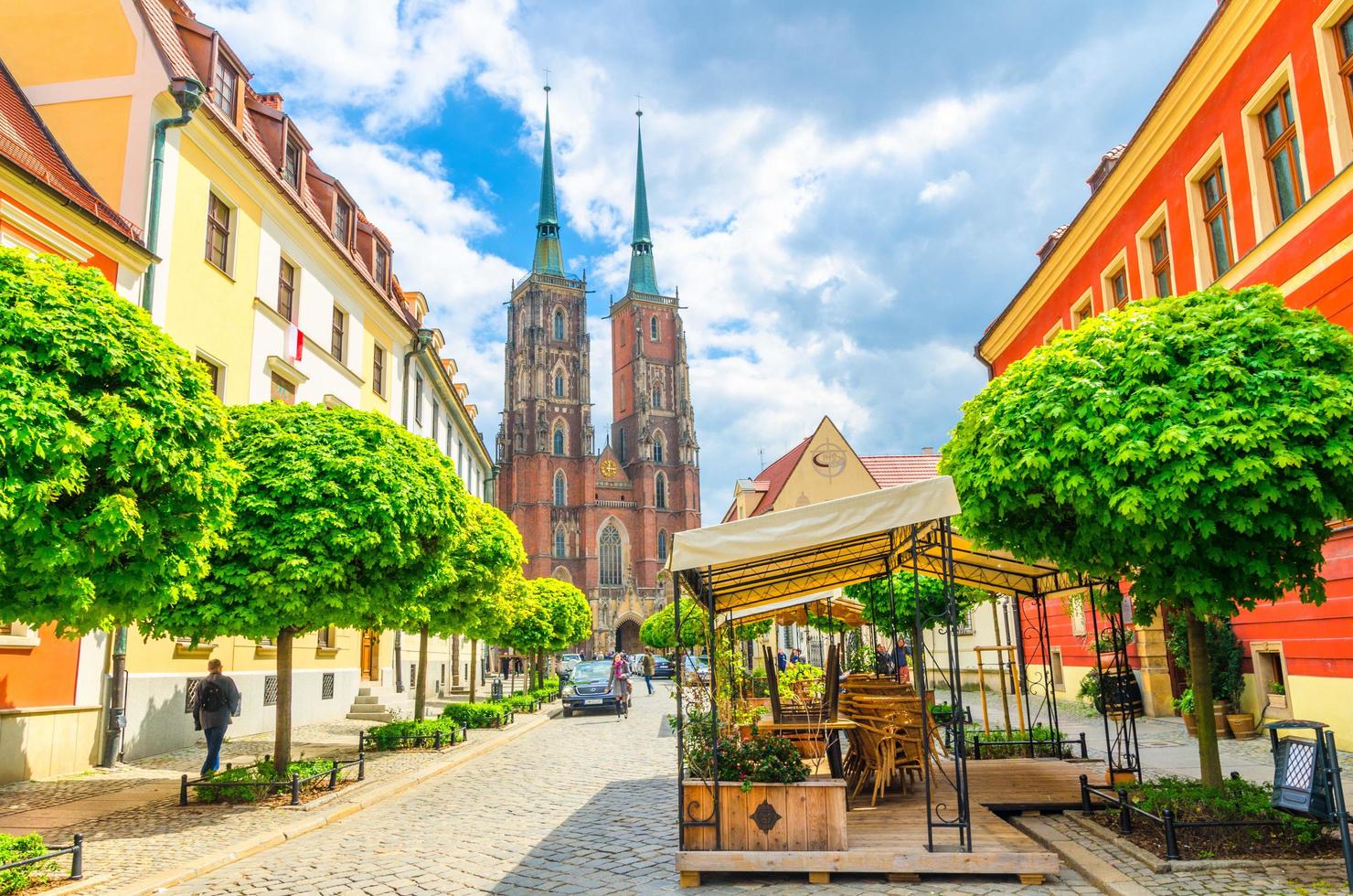 Wroclaw, Poland, May 7, 2019 Street with cobblestone road with green trees, colorful buildings, Cathedral of St. John the Baptist church with two spires in old historical city centre, Ostrow Tumski photo