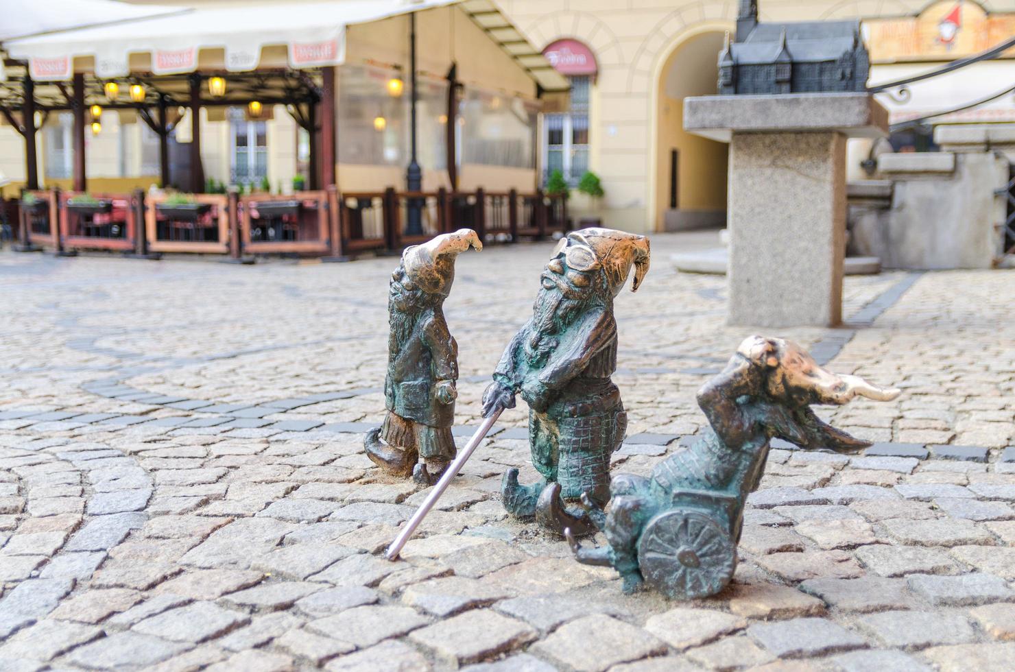 Wroclaw, Poland, May 7, 2019 three Dwarfs deaf, blind with a stick and invalid in a wheelchair, famous bronze miniature gnome with hat sculpture is a symbol of Wroclaw in old historical city centre photo