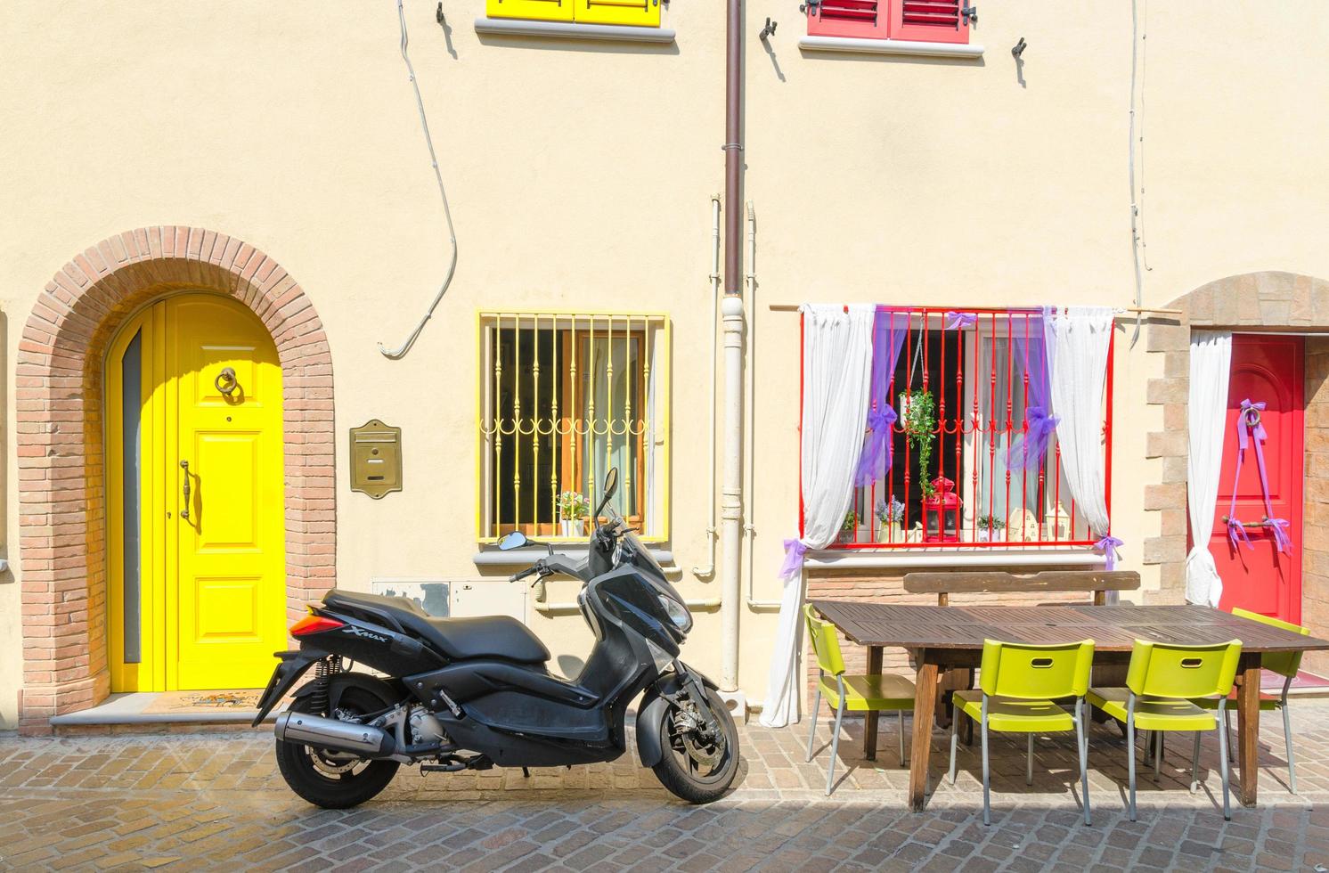 rimini, italia, 19 de septiembre de 2018 mesa con sillas y moto scooter estacionado en una calle adoquinada cerca de edificios con paredes coloridas, puertas y ventanas en el centro histórico de la ciudad foto