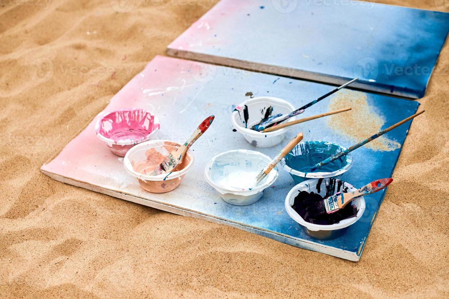 Two painted canvas with palettes of paints lying on sand, artist's palette at outdoor art festival photo