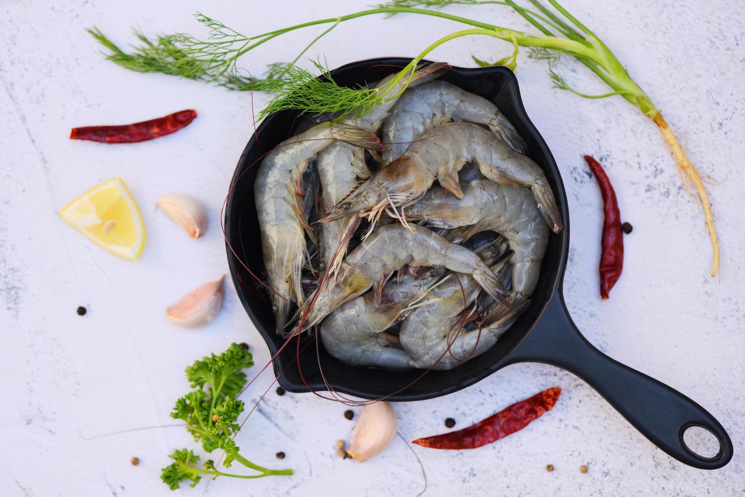 Fresh shrimp prawns for cooking with spices lemon on dark background in the seafood restaurant, raw shrimps on pot, top view photo