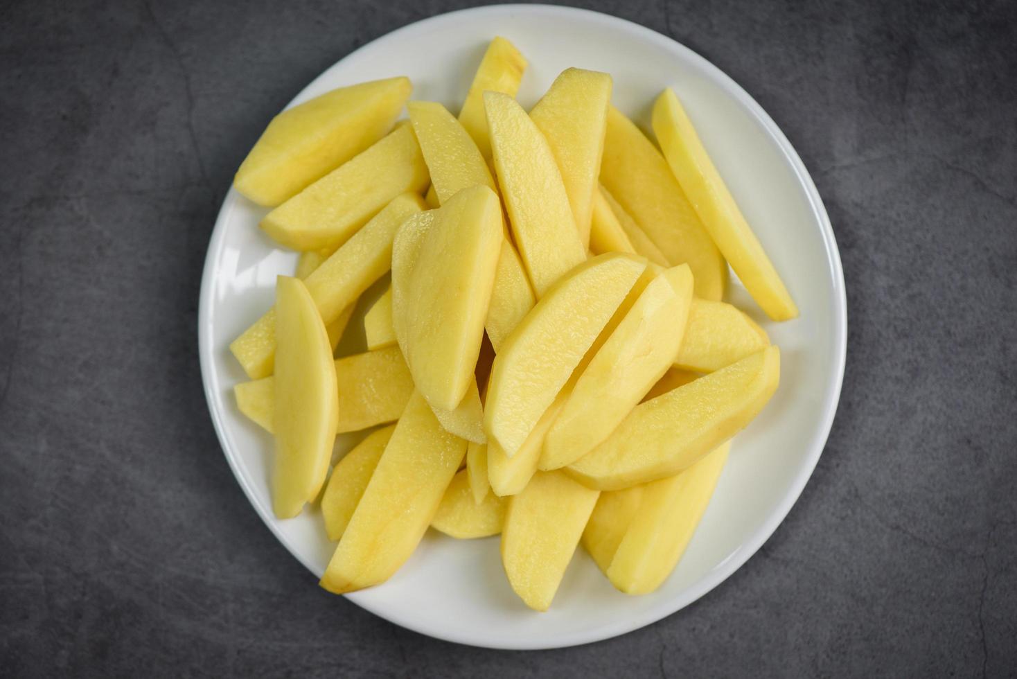 gajos de patata cruda fresca, patatas picadas para comida cocinada en plato blanco foto