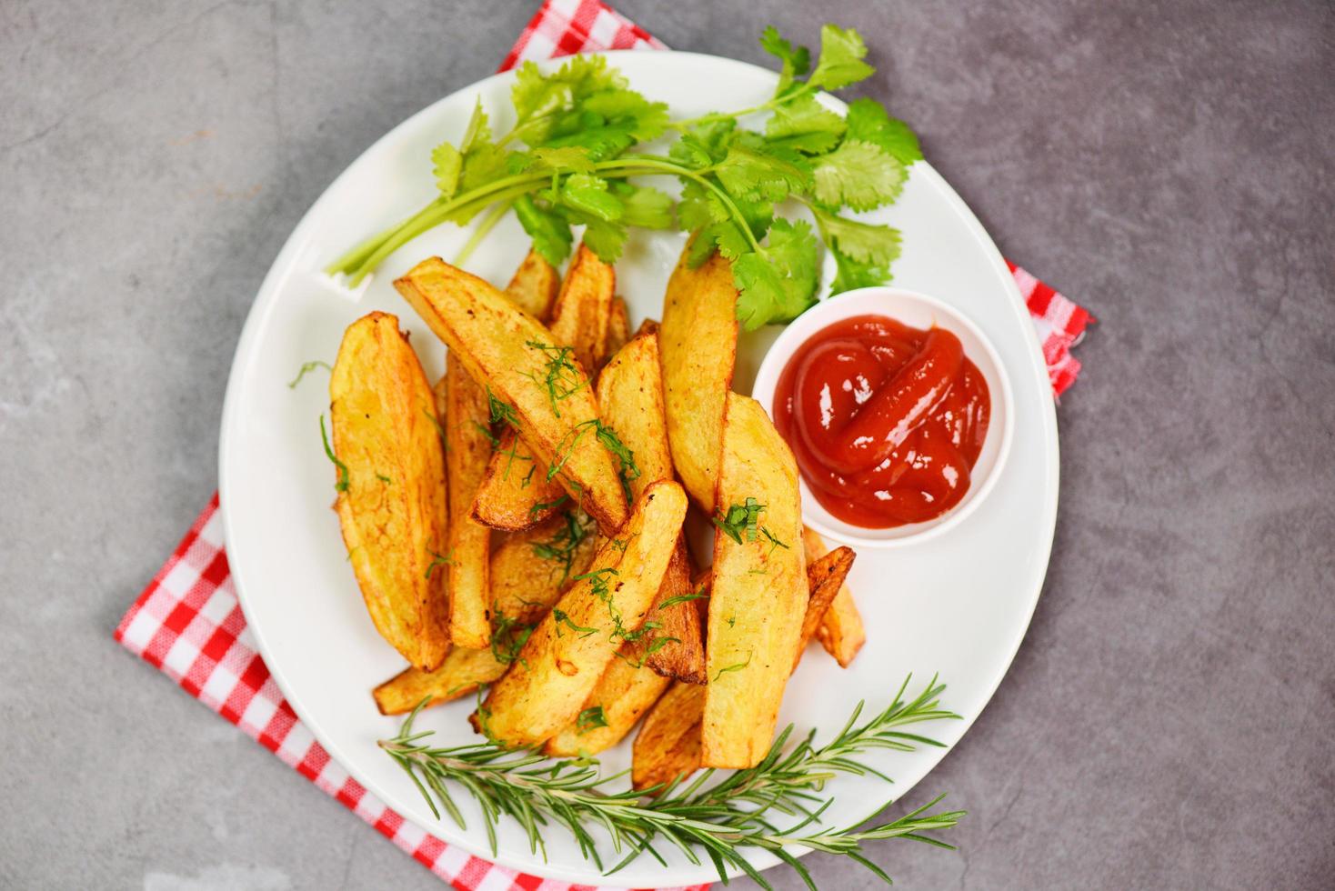 gajos de patata en un plato blanco con cilantro de hierbas de romero y salsa de ketchup de tomate, cocinando patatas fritas o patatas fritas foto