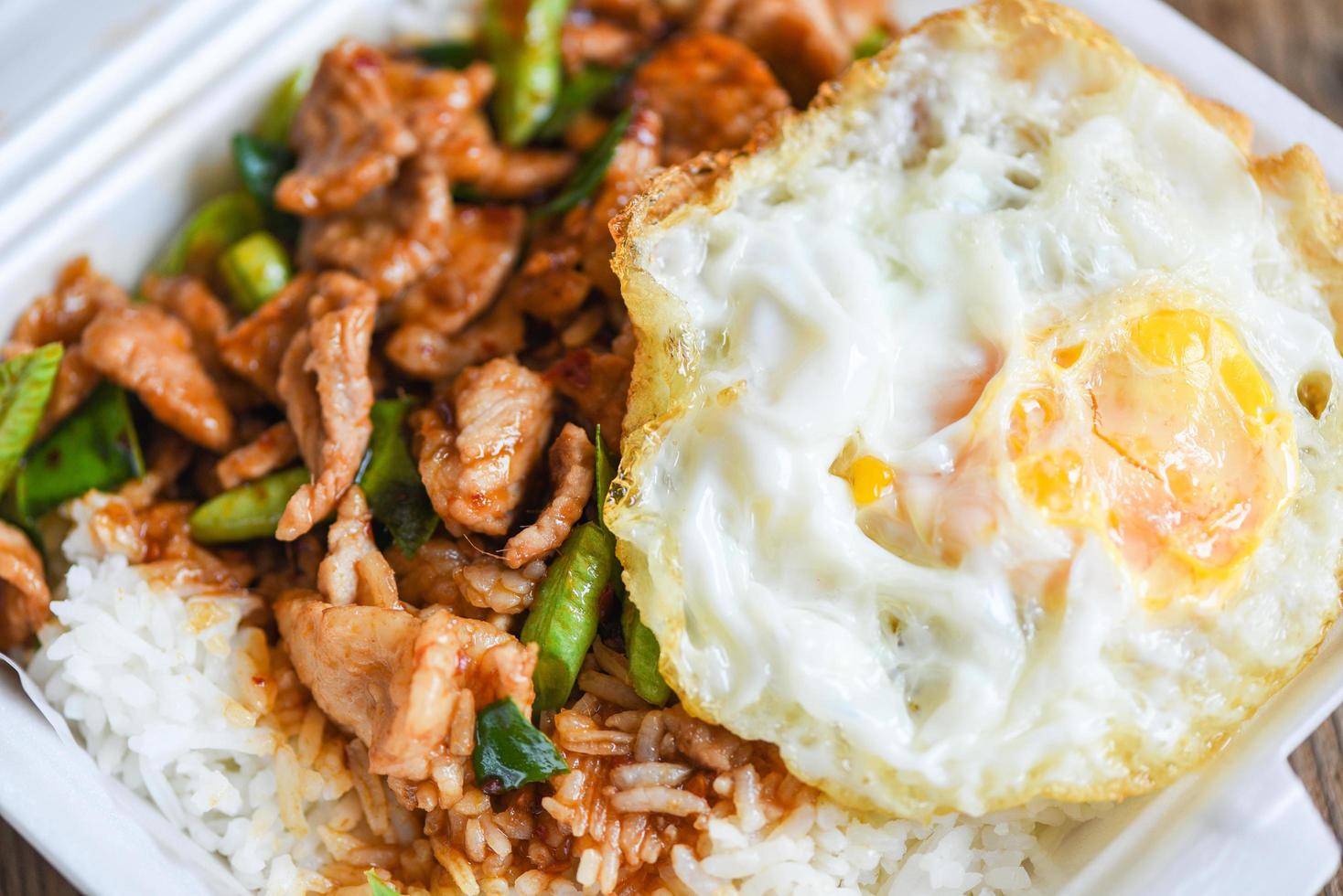 Stir fried pork with red curry paste and basil leaves with yardlong bean and fried egg topped in a plastic box, Thai food or Thai street food photo