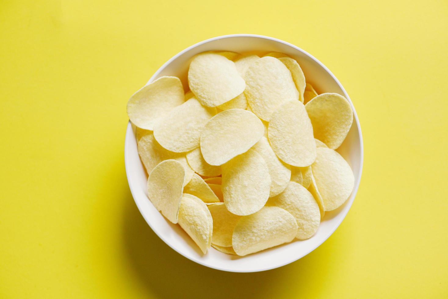 Potato chips snack on bowl and yellow background, Crispy potato chips on the kitchen photo