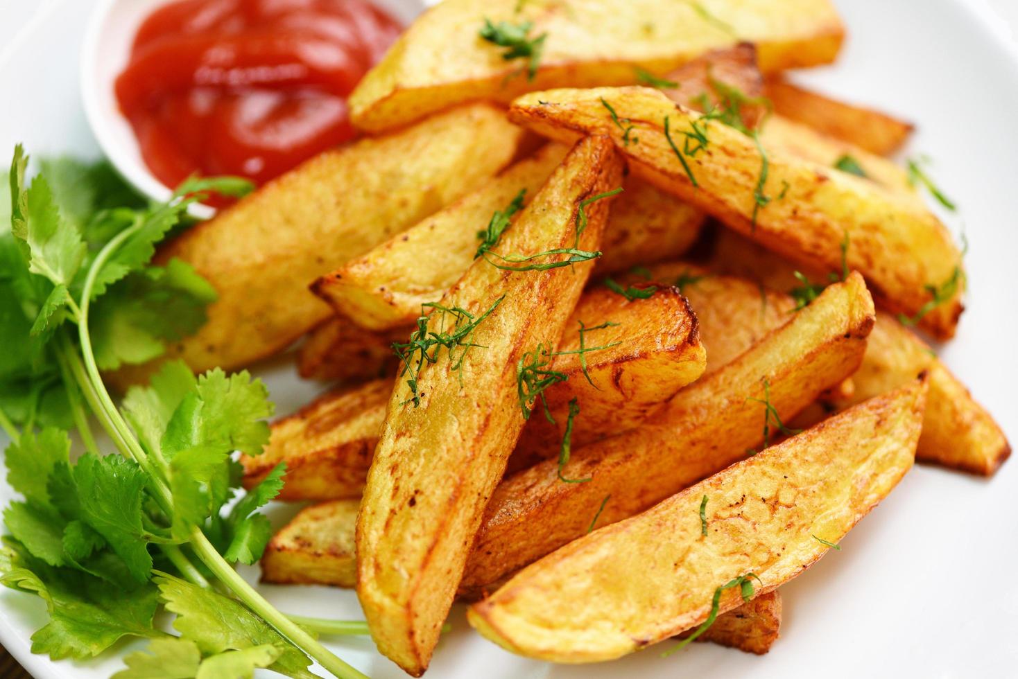 gajos de patata en un plato blanco con cilantro de hierbas de romero y salsa de ketchup de tomate, cocinando patatas fritas o patatas fritas foto