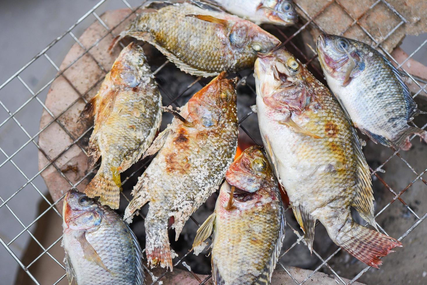 pescado a la parrilla a la parrilla, pescado de tilapia a la parrilla con sal para cocinar pescado quemar comida tailandesa foto