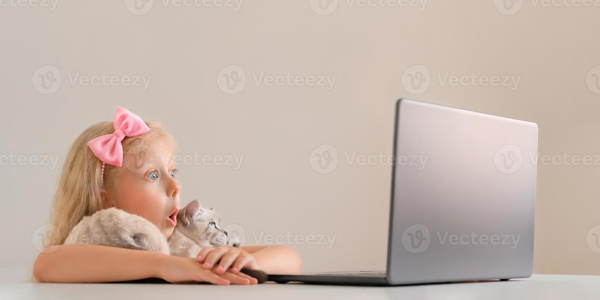 Cute little girl hugs her cat and looks curiously at her laptop. photo