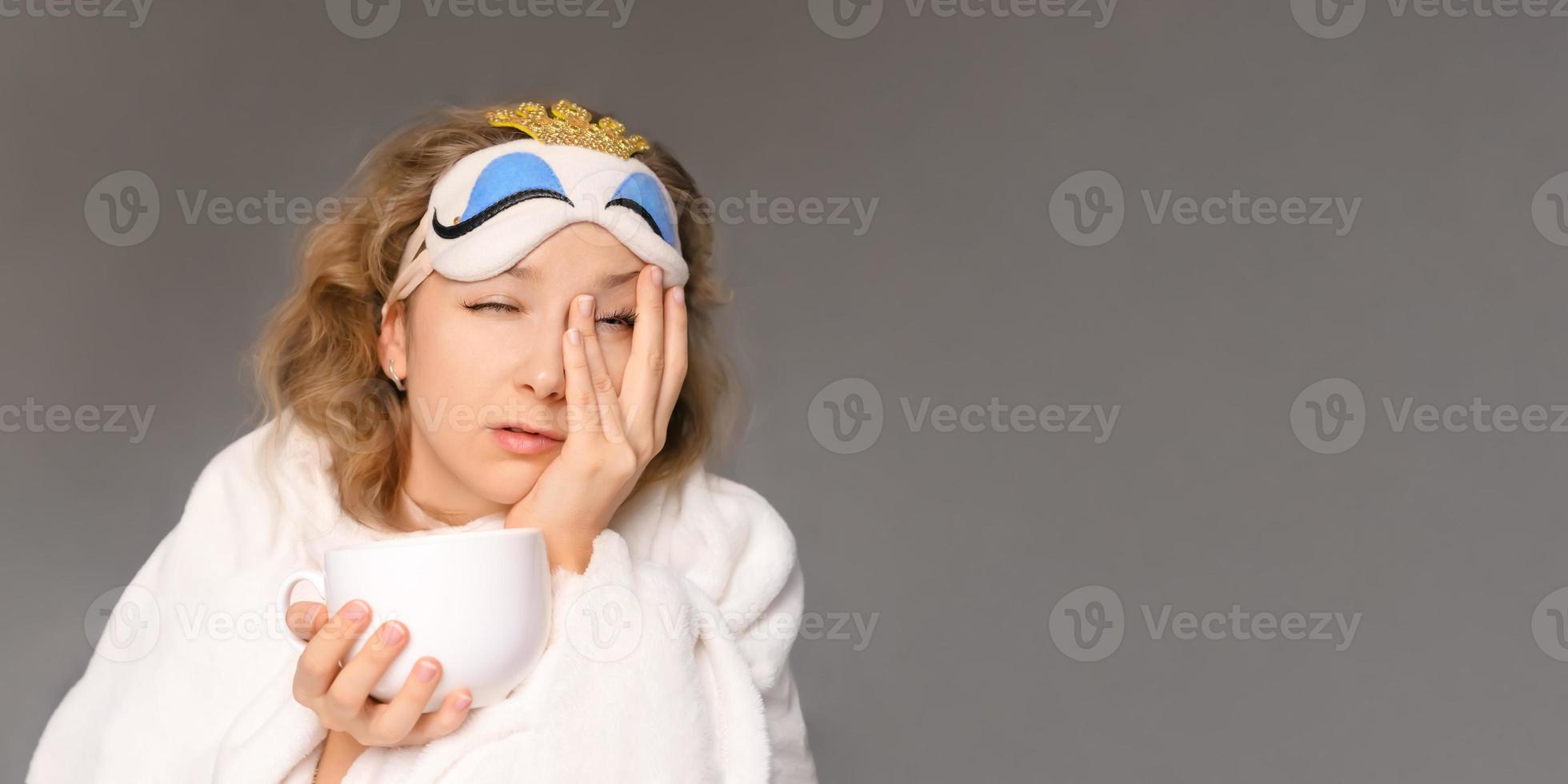 una mujer con una máscara para dormir intenta despertarse mientras bebe café foto