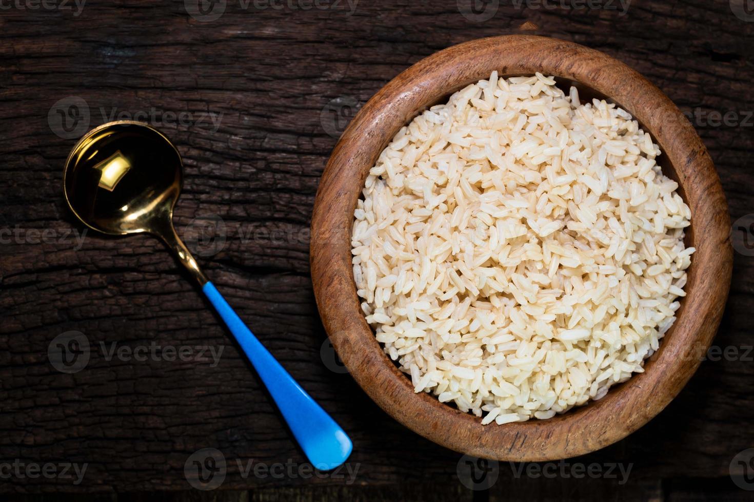 el arroz marrón en un tazón tiene una cuchara aislada en el fondo de madera foto