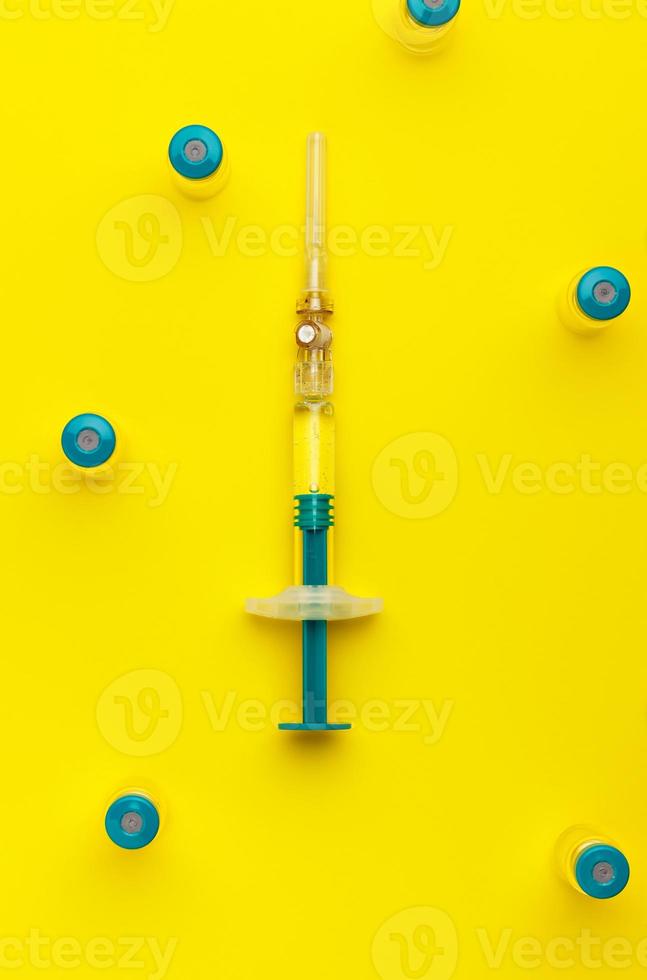 Syringe with several medical vials for injecting on yellow background. Top view. photo