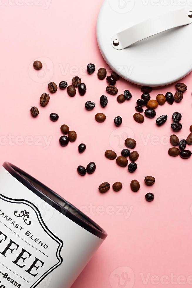 Coffee beans out of coffee pot with pot lid next to it on pink background. photo