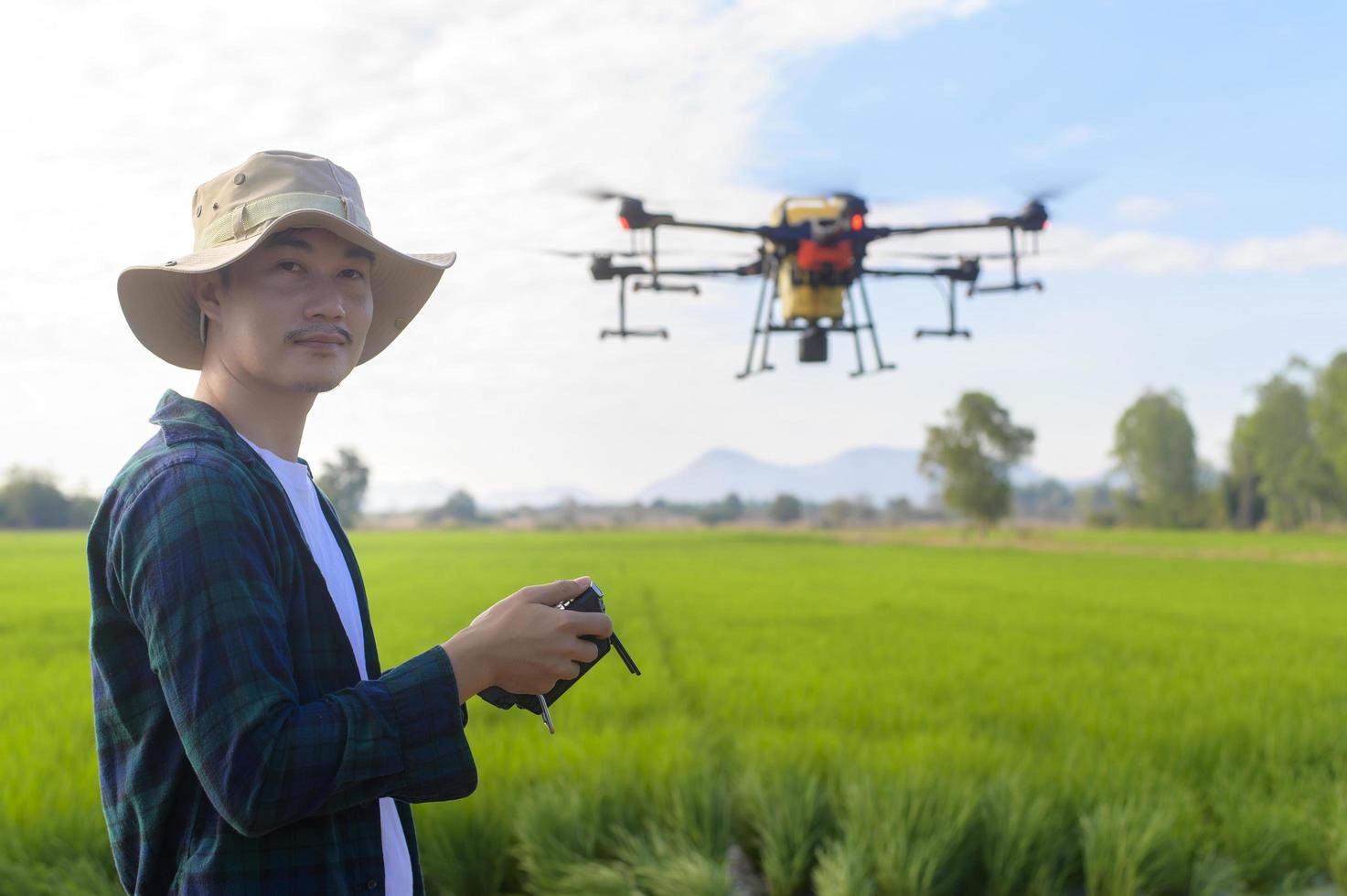 Young smart farmer controlling drone spraying fertilizer and pesticide over farmland,High technology innovations and smart farming photo