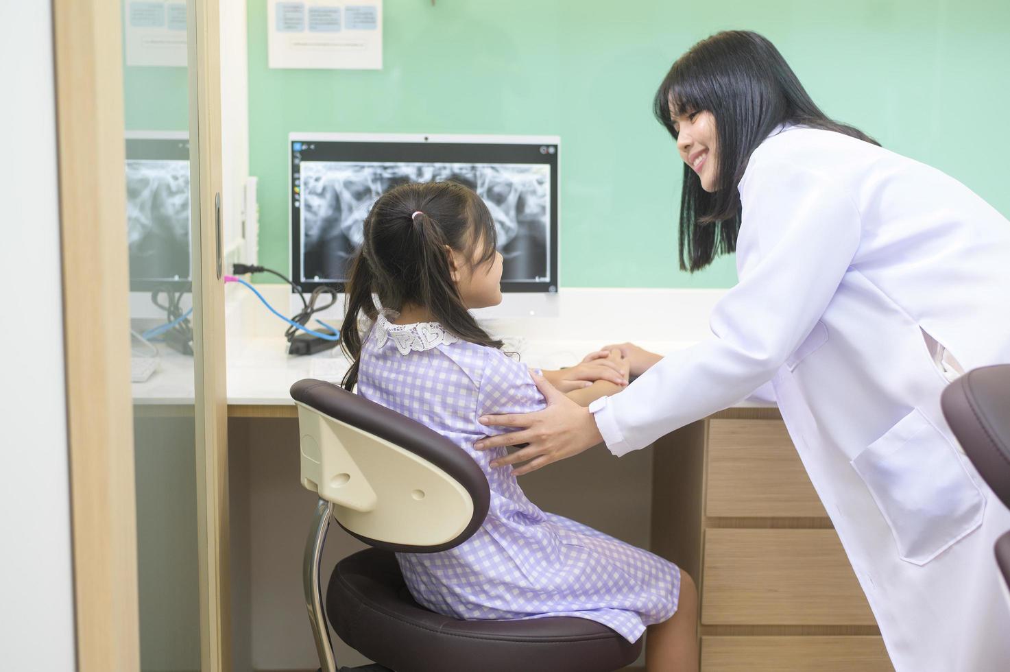 mujer dentista explicando la radiografía de los dientes a una niña en la clínica dental, chequeo dental y concepto de dientes sanos foto