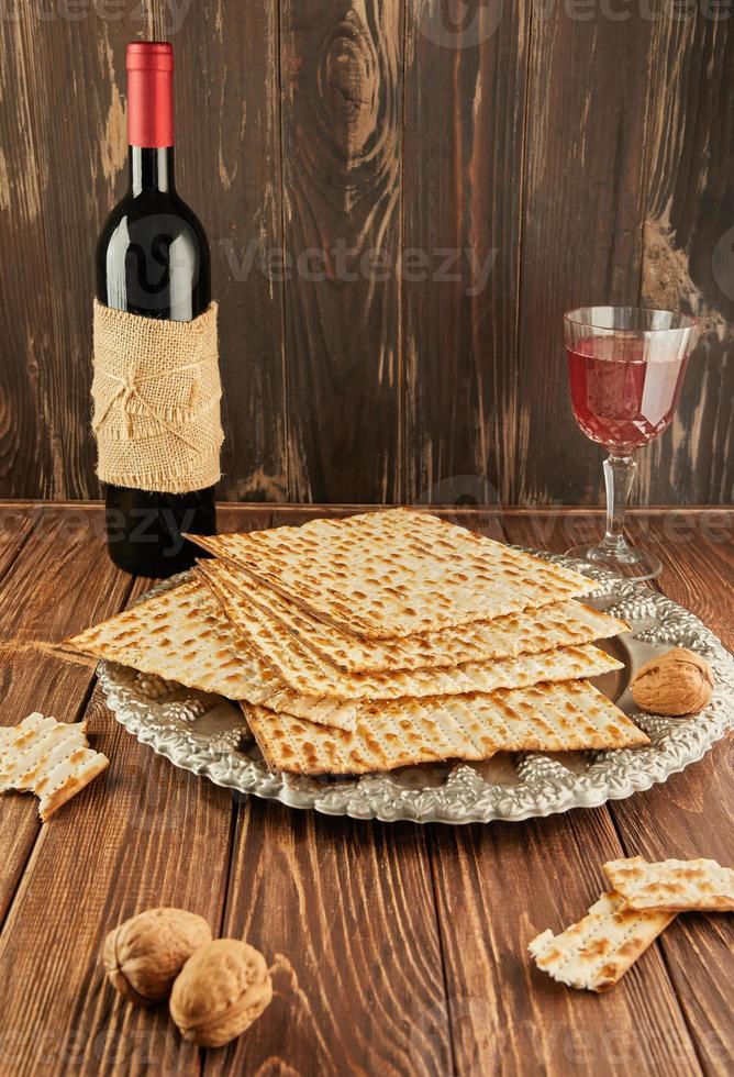 concepto de celebración de pesach - festividad judía pesach. matzá en plato tradicional de seder con botella de vino tinto, copa de vino y nueces sobre fondo vintage de madera foto