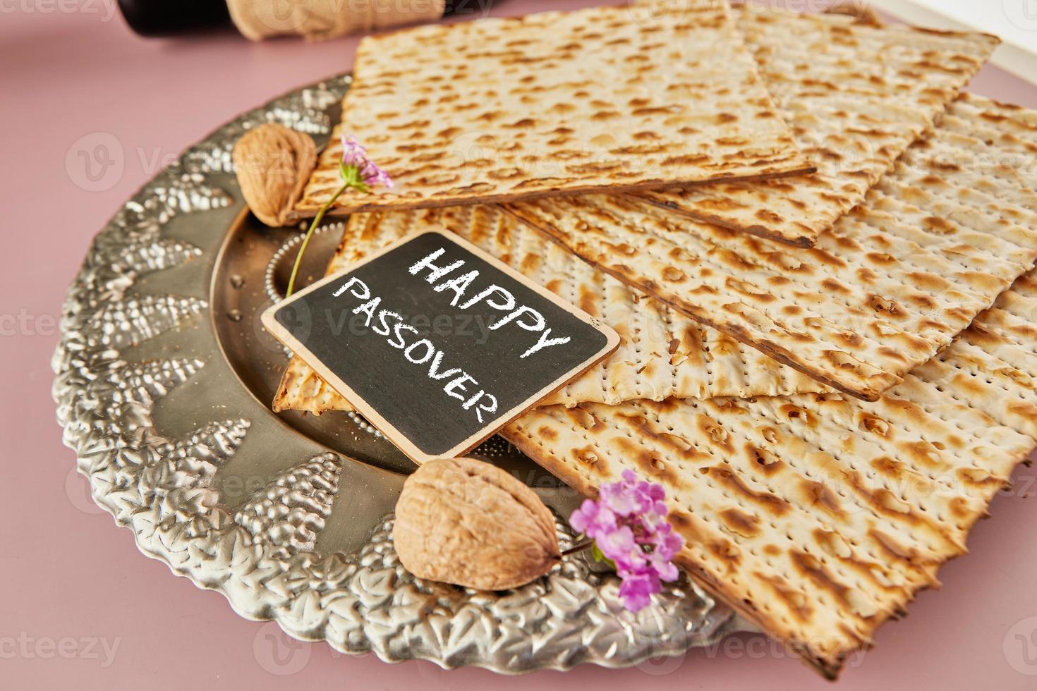 Pesach celebration concept - Jewish holiday Pesach. Matzah on traditional Seder plate with bottle of red wine, nuts on purple background and the inscription Happy Passover photo
