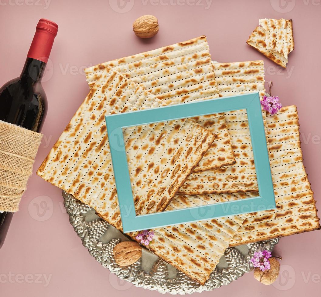 Pesach celebration concept - Jewish holiday Pesach. Matzah on traditional Seder plate with bottle of red wine, nuts on purple background and blue frame for text photo