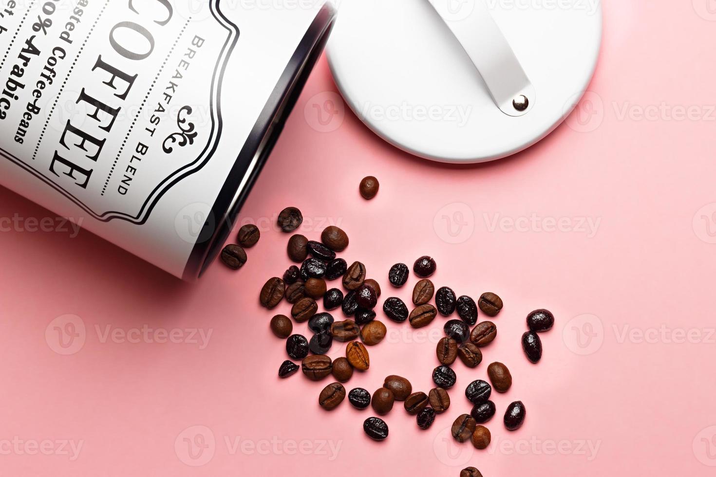 Coffee beans out of coffee pot with pot lid next to it on pink background. photo