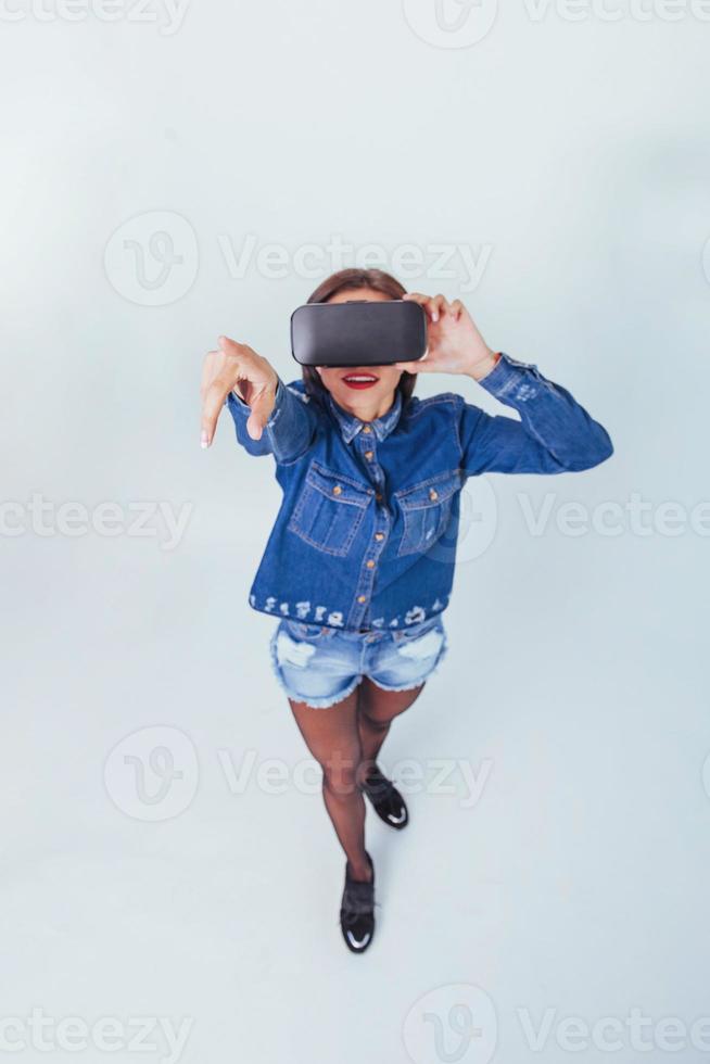 brunette beautiful woman posing in the studio, wearing jeans wear, using VR-glasses virtual reality headsets photo