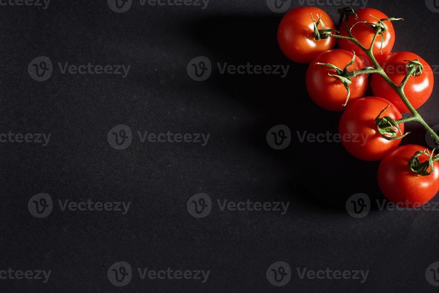 Branch of red organic tomatoes on a black background. photo
