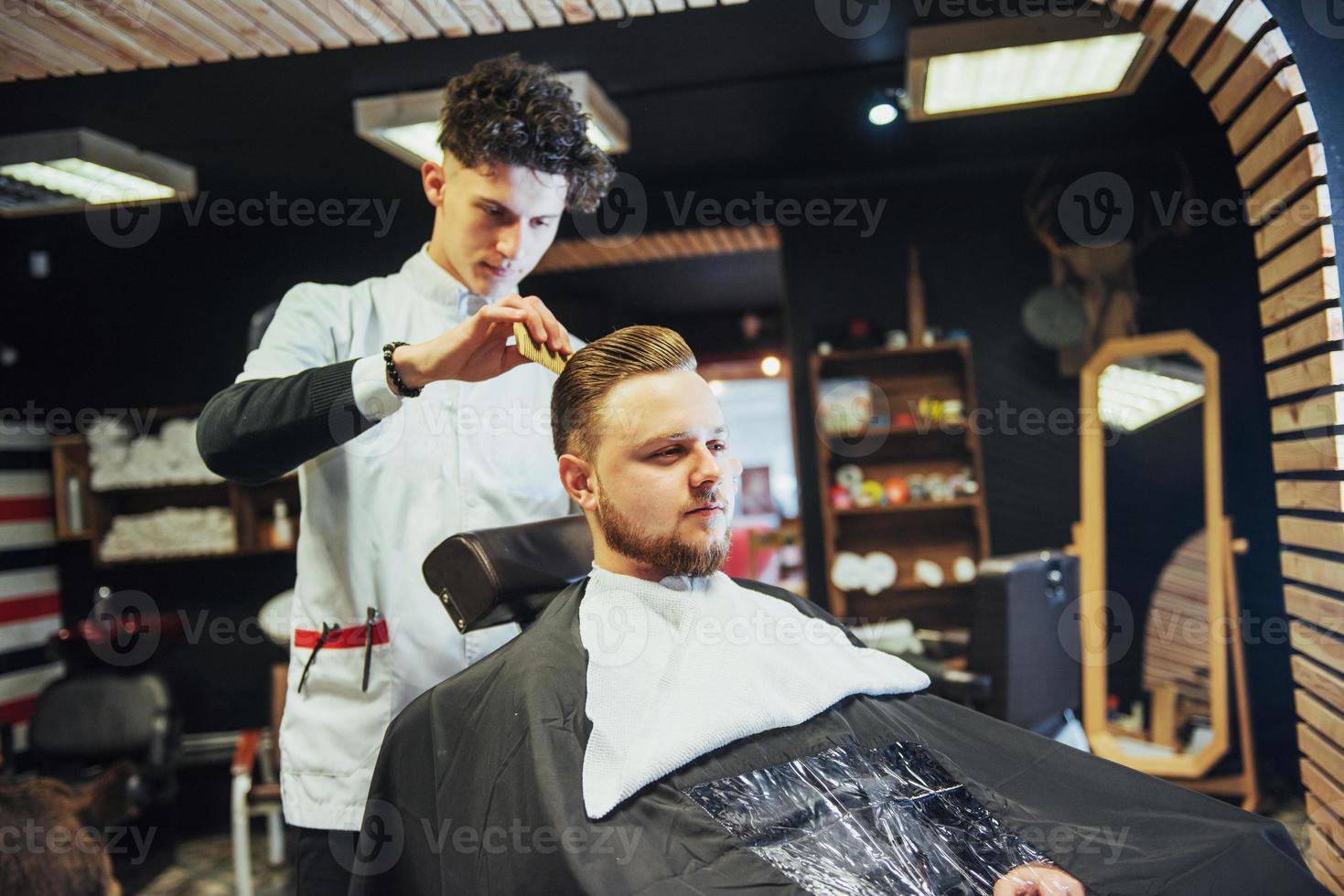 el peluquero en el proceso de cortar la barba de las cortadoras eléctricas del cliente foto