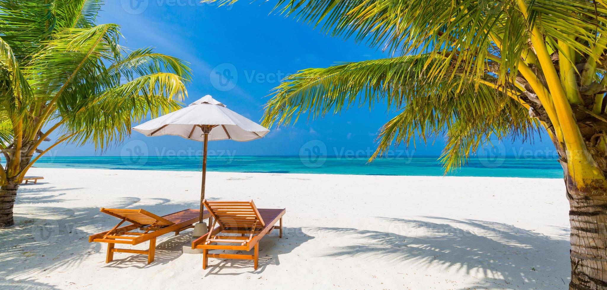 Beautiful tropical island scenery, two sun beds, loungers, umbrella under palm tree. White sand, sea view with horizon, idyllic blue sky, calmness and relaxation. Inspirational beach resort hotel photo