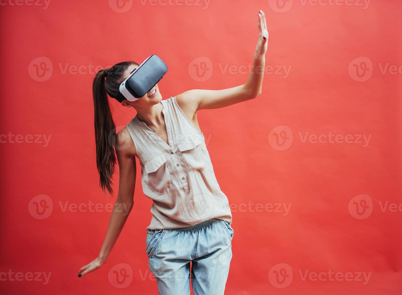 A young woman with a VR device on a red background in studio photo