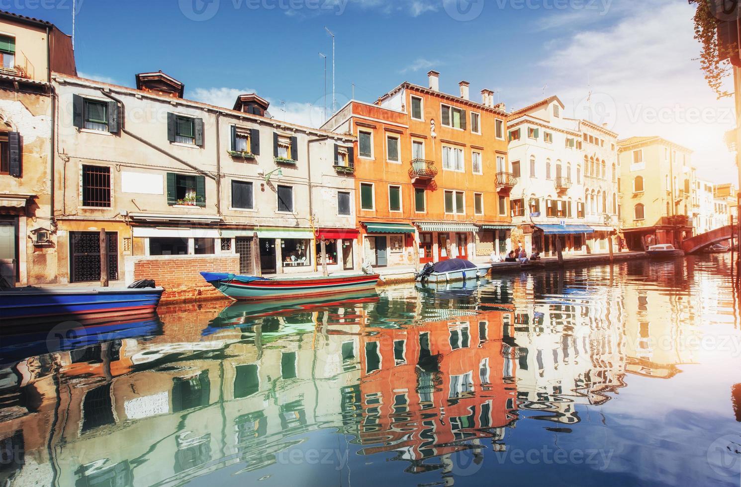 canal de agua verde con góndolas y coloridas fachadas de antiguos edificios medievales al sol en venecia, italia. foto